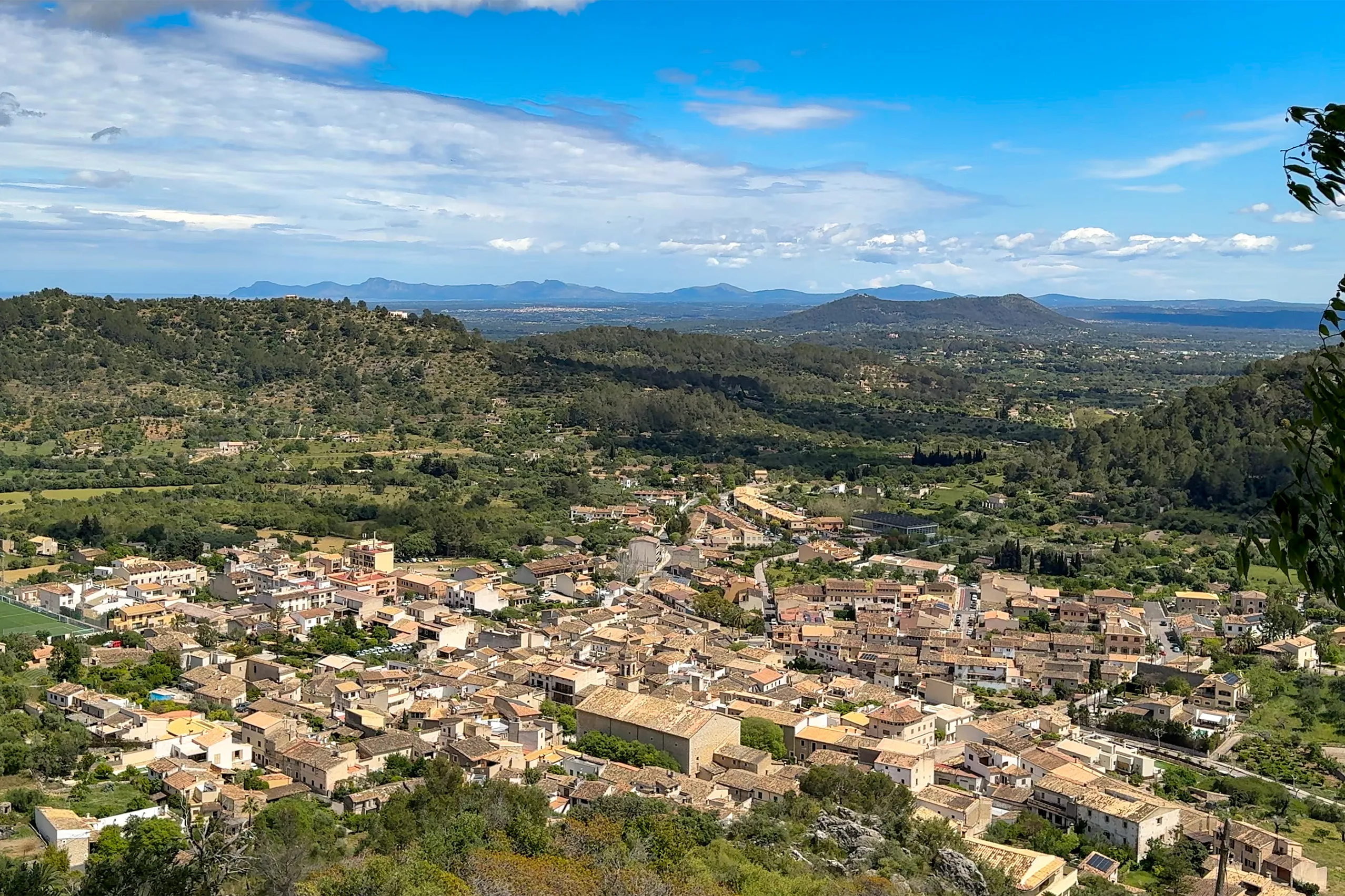 Weiter Blick von Santa Llúcia über die Dächer von Mancor de la Vall und die bewaldete Ebene bis zu den Bergen am Horizont.
