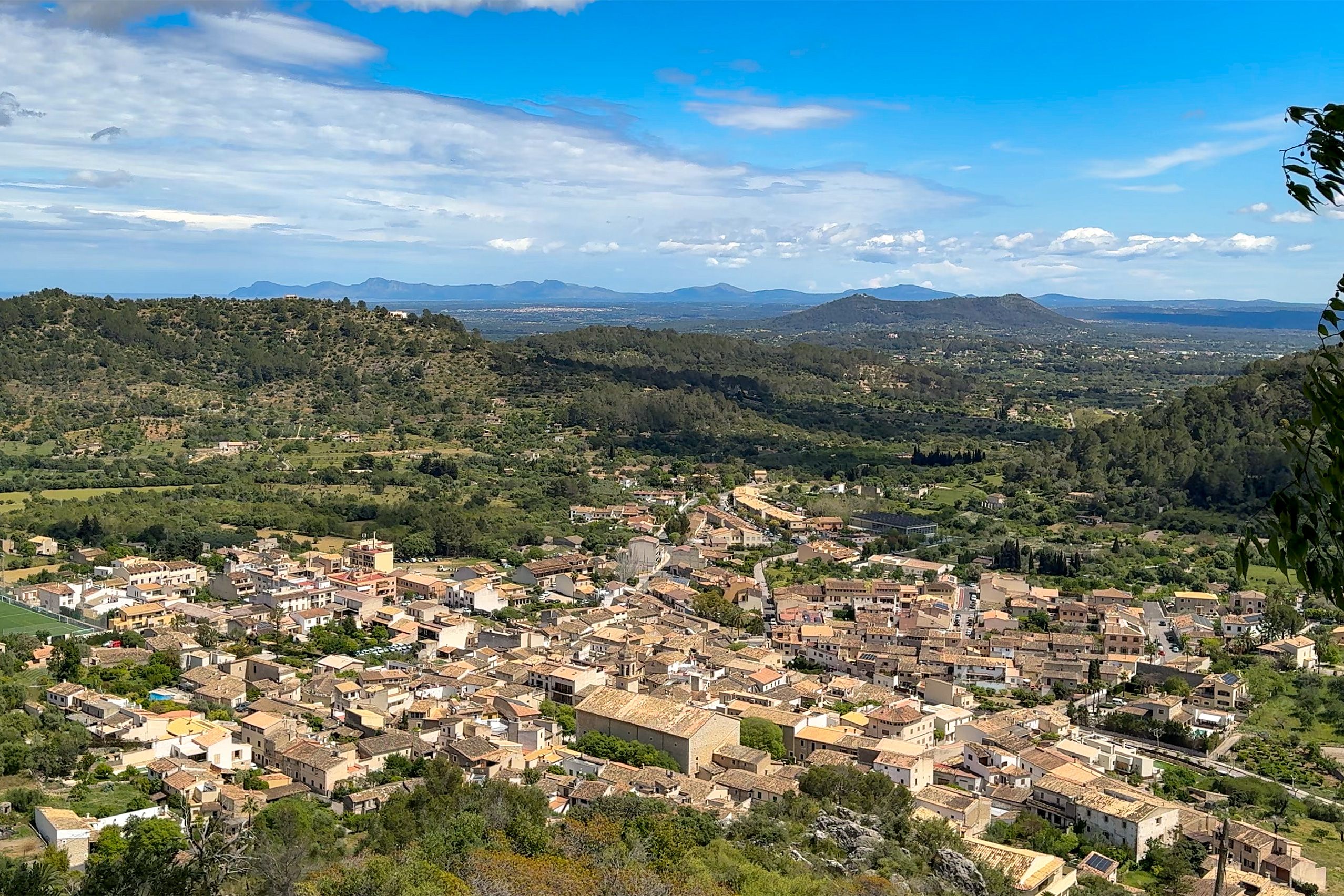 Weiter Blick von Santa Llúcia über die Dächer von Mancor de la Vall und die bewaldete Ebene bis zu den Bergen am Horizont.
