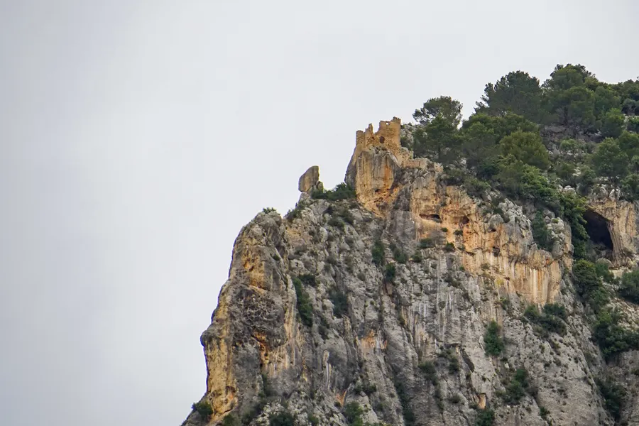 Blick von oben über die senkrechte Felskante des Puig d'Alaró hinunter auf bewaldete Hänge und die Ebene im Dunst.
