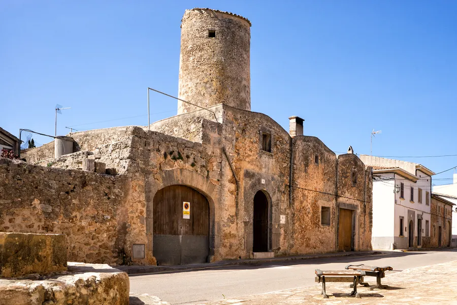 Runder Turm einer alten Windmühle aus Bruchstein mit Ziegelkappe am Carrer de sa Quarterada in Algaida, an dessen Fuß Wohn- und Wirtschaftsgebäude mit Rundbogentoren angebaut sind.