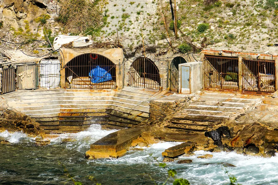 Alte gewölbte Bootshäuser mit Gittertoren direkt am Wasser unterhalb von Banyalbufar, davor eine Steinrampe und Brandung.

