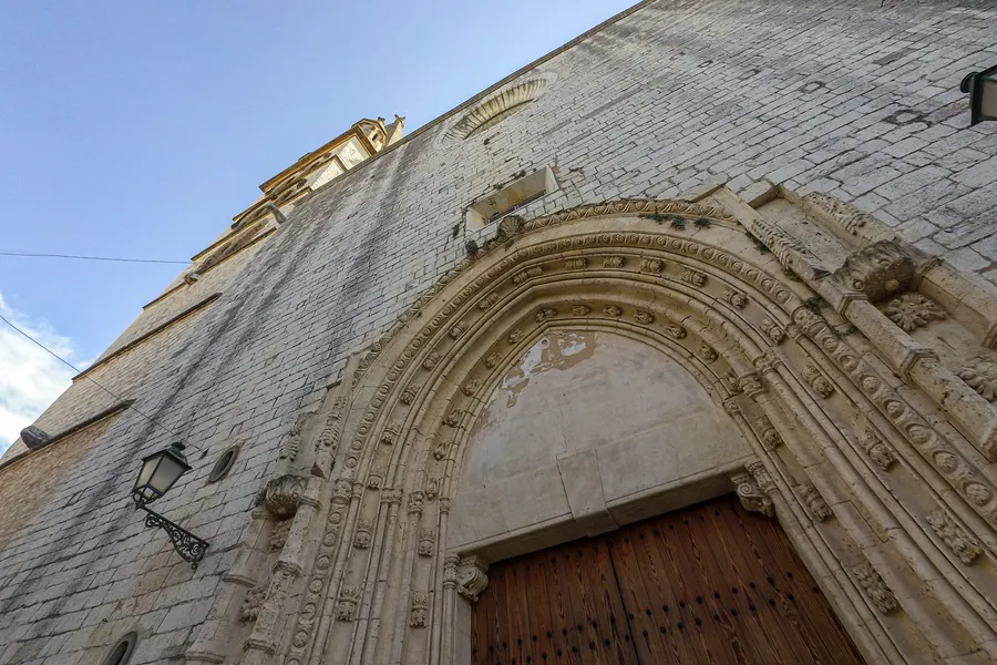 Das reich profilierte gotische Spitzbogenportal der Kirche von Binissalem mit hölzernem Tor, von schräg unten aufgenommen.
