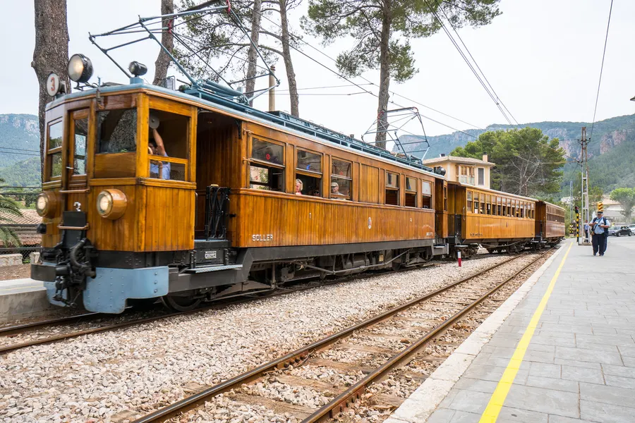 Historischer hölzerner Triebwagen mit Stromabnehmer und runden Scheinwerfern auf dem Gleis, dahinter weitere Wagen.
