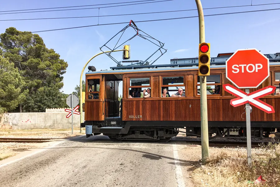 Historischer Triebwagen an einem Bahnübergang in Bunyola, davor Stoppschild, Andreaskreuz und Ampel.
