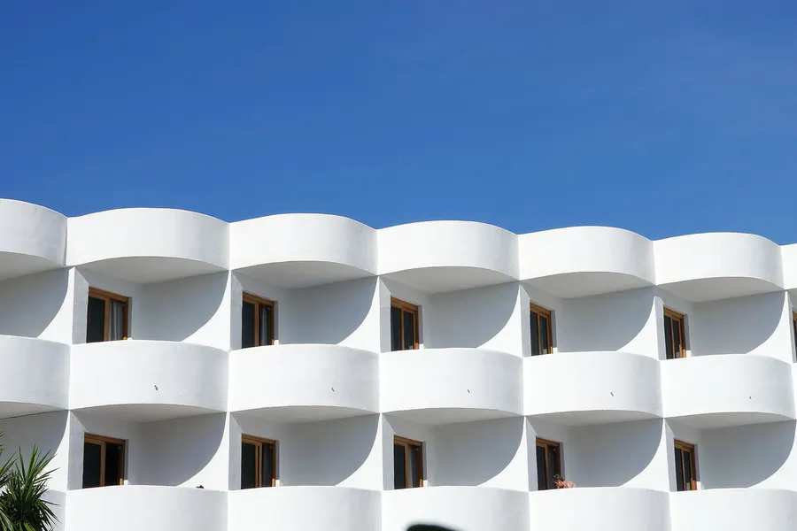 Weiße, kubische Apartmentanlage in Cala d'Or mit gestaffelten Balkonen und Rundbögen, ganz in Weiß gehalten.
