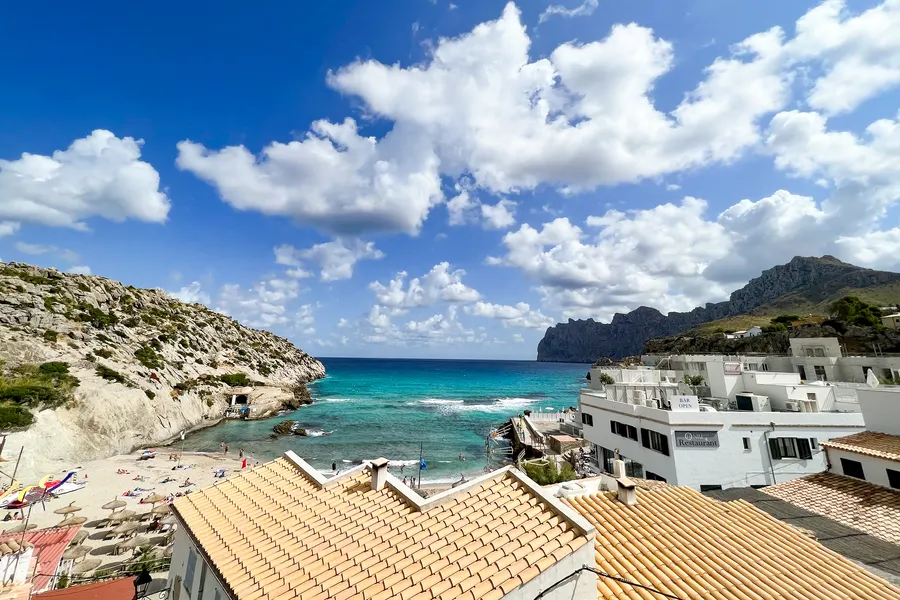 Blick über die Dächer von Cala de Sant Vicenç auf die Bucht, rechts der gezackte Felskamm des Cavall Bernat, der steil ins Meer abfällt.