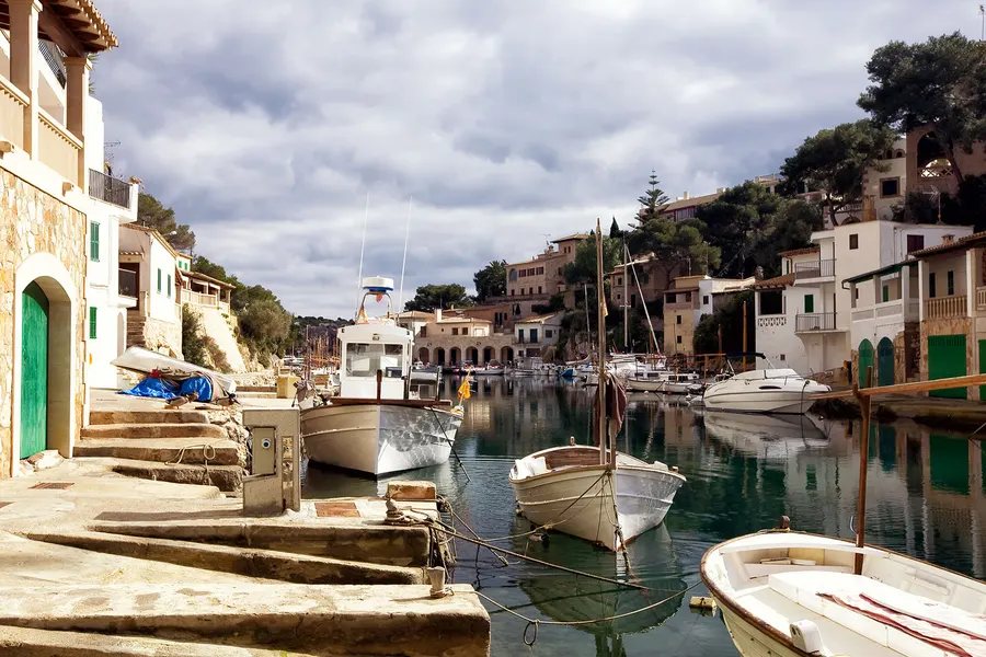 Wohnhäuser mit Terrassen dicht über dem Wasser des Meeresarms von Cala Figuera, davor liegende Boote und Stege.