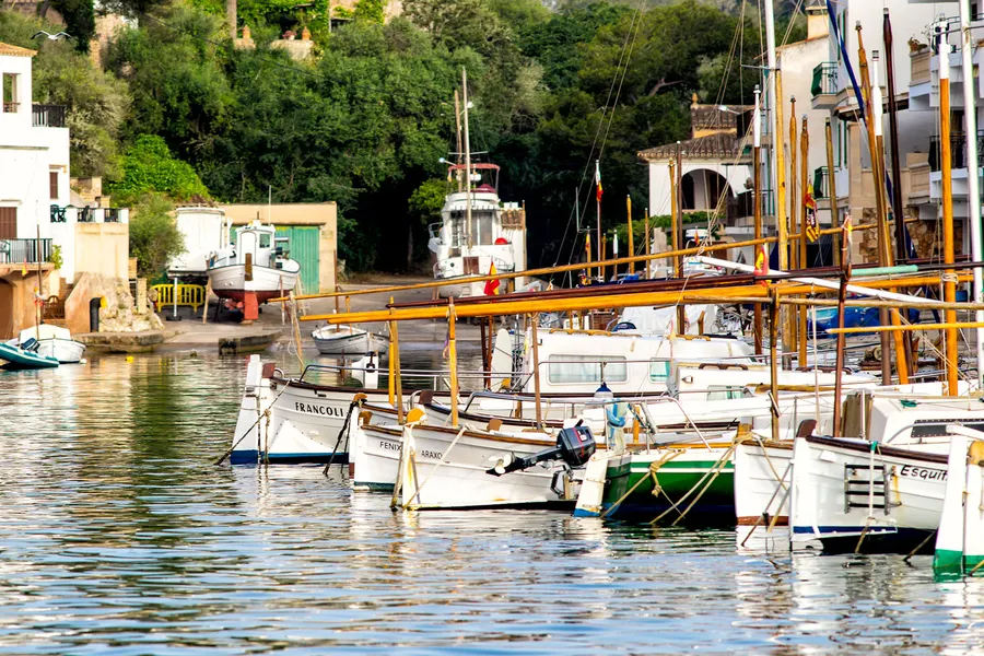 Dicht liegende Fischerboote mit Ausrüstung am Kai von Cala Figuera, im Hintergrund Bootshäuser und die bewachsene Felswand.