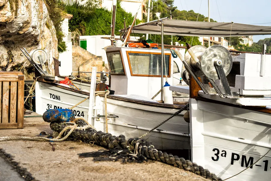 Weißes Fischerboot mit Kennzeichen auf einer gepflasterten Slipanlage an Land gezogen, daneben aufgerolltes Tauwerk.
