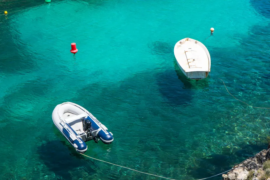 Zwei kleine Boote vor Anker im leuchtend türkisfarbenen Wasser der Cala Fornells über hellem Sandgrund.