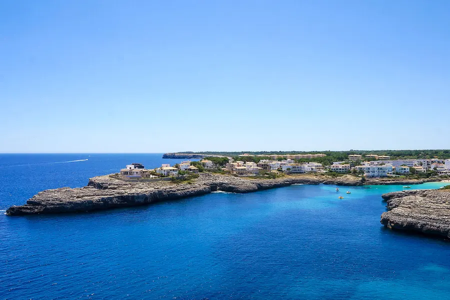 Blick über die flache Felsküste bei Portocolom mit tiefblauem Wasser und den weißen Häusern auf der Landzunge.