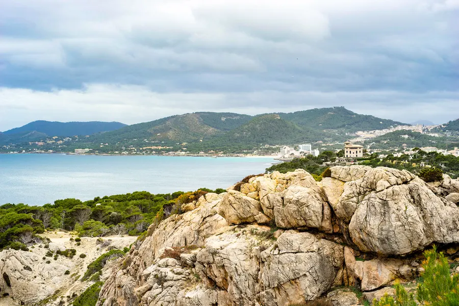 Blick von einer Felskuppe über die Küste bei Cala Ratjada auf eine weite Bucht und die bewaldeten Hügel des Hinterlands.
