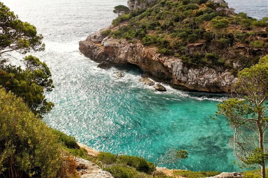 Blick über die zerklüftete Felskante bei Caló des Moro auf das türkisfarbene Wasser der Bucht und die vorgelagerten Klippen.