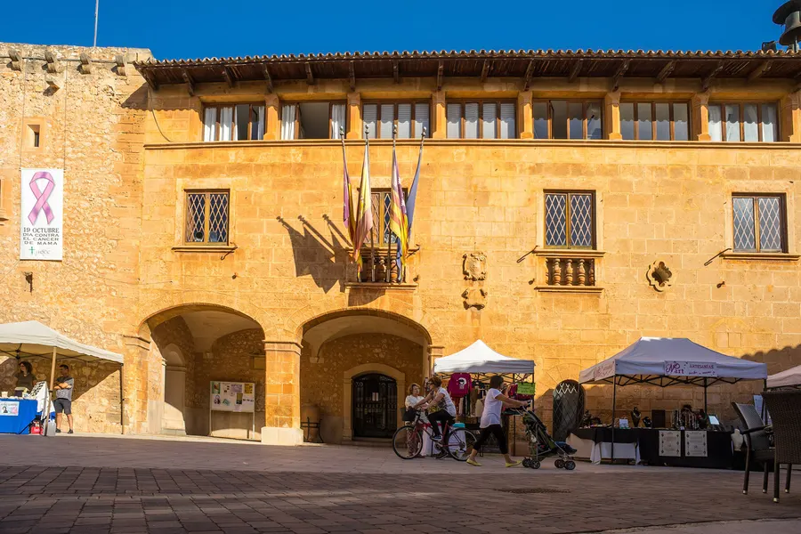 Das Rathaus von Campos aus Sandstein mit hölzernem Dachüberstand, Fahnen und Bogengang, davor Marktstände unter Schirmen.