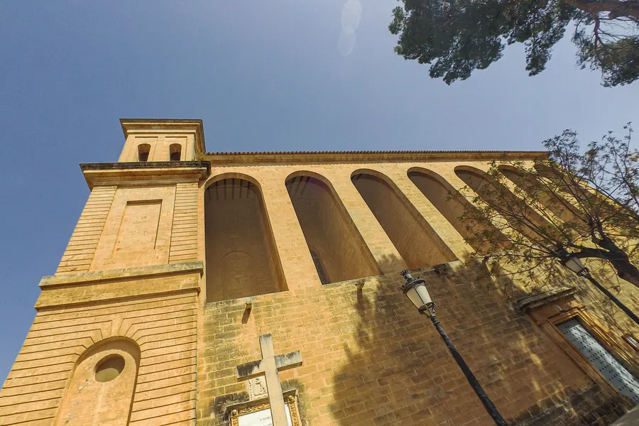 Die hohe Sandsteinwand der Kirche von Campos mit einer Reihe von Strebebögen, von unten gegen den Himmel aufgenommen.
