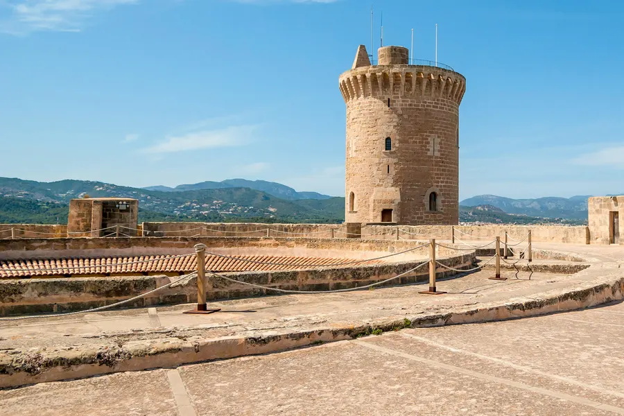 Blick über den umlaufenden Graben des Castell de Bellver auf Mauerkrone und Hauptturm, im Hintergrund die Berge hinter Palma.
