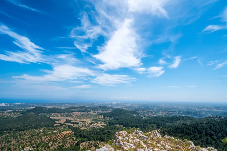 Weiter Blick vom Castell de Santueri über bewaldete Hänge und die Ebene des Ostens bis zum Meer am Horizont.
