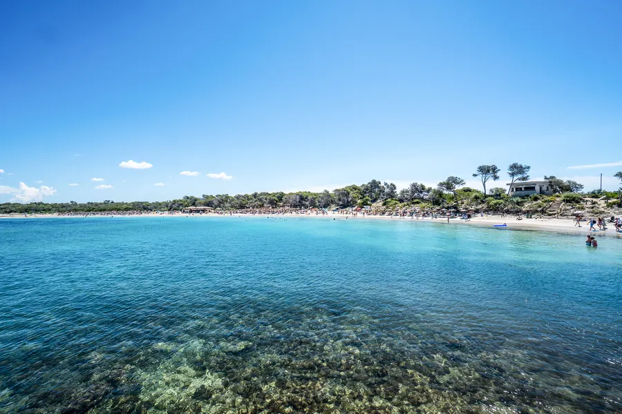 Sandstrand direkt am Ort mit Badenden im flachen Wasser, Sonnenschirmen und den Häusern der Promenade dahinter.
