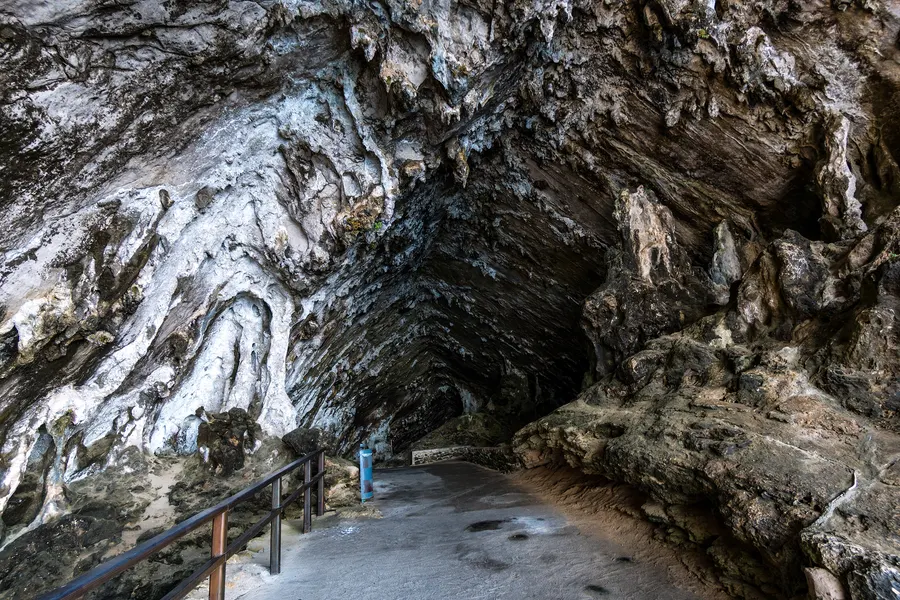 Die zerklüftete Felsdecke im Eingangsbereich der Coves d'Artà mit hellen Kalkadern und einem befestigten Weg mit Geländer.