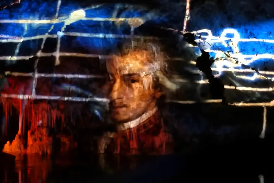 Auf die Höhlenwand projiziertes Porträt Mozarts in blauem und rotem Licht, davor die Silhouetten der Tropfsteine.