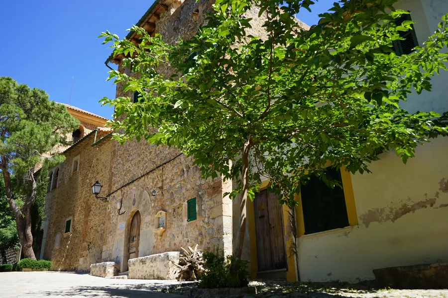Steinernes Tor mit schmiedeeisernem Gitter am Zugang zum Friedhof von Deià, dahinter die Hänge der Tramuntana.
