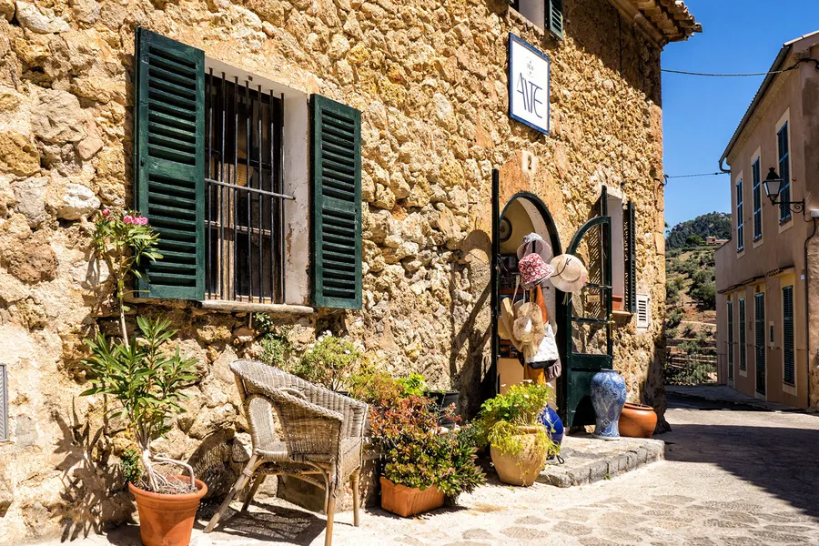 Steinhaus in Deià hinter einer hohen Trockenmauer, davor ein alter Olivenbaum mit weit ausladenden Ästen.
