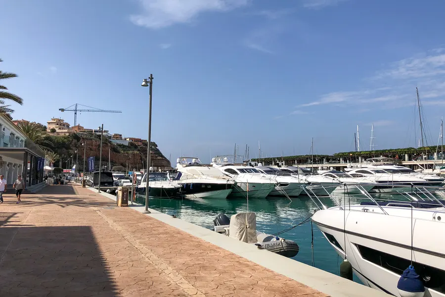 Reihe großer weißer Motoryachten an den Stegen von Port Adriano unter blauem Himmel.
