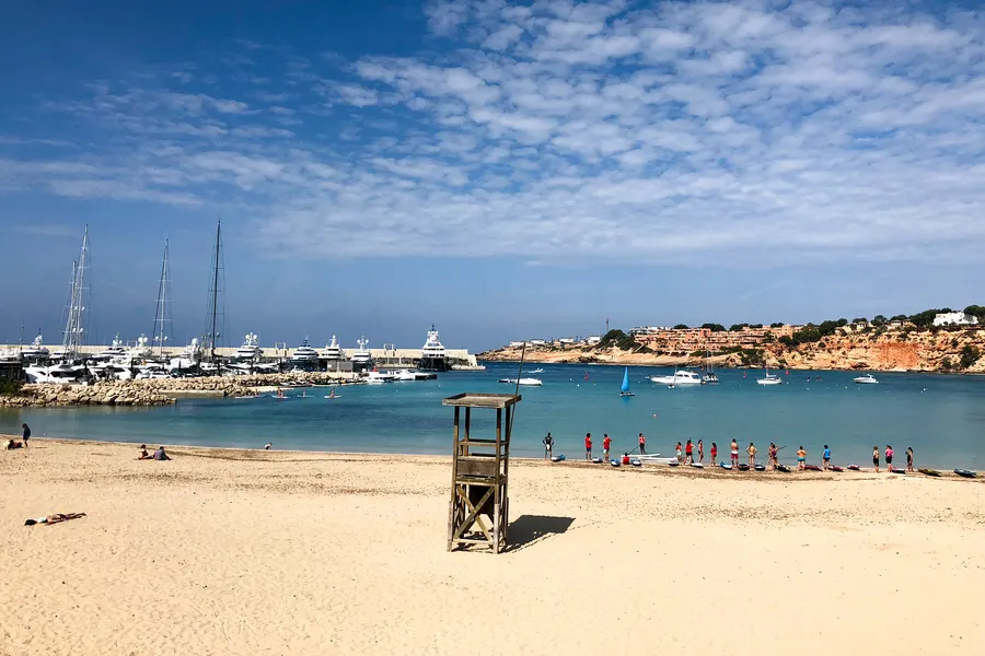 Sandstrand von El Toro mit Rettungsturm, ruhigem flachem Wasser und Booten in der Bucht dahinter.
