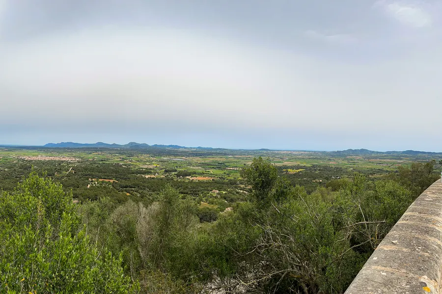 Weiter Blick von der Ermita de Bonany über die grüne Ebene des Pla de Mallorca mit Feldern, Dörfern und fernen Hügelketten.
