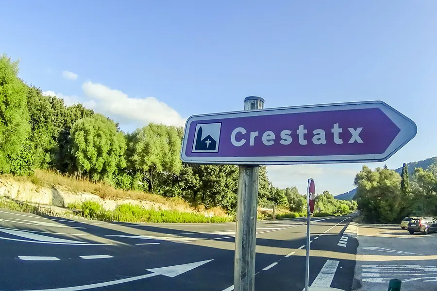 Breiter Weg aus unregelmäßigen Steinplatten, der zwischen Bäumen und Sträuchern zur Kapelle von Crestatx hinaufführt.