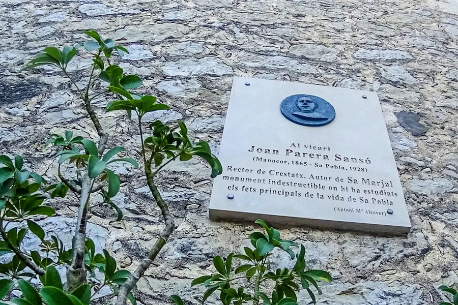 Steinerne Gedenktafel an der Mauer der Kapelle von Crestatx mit eingemeißelter Inschrift und einem Porträtmedaillon.
