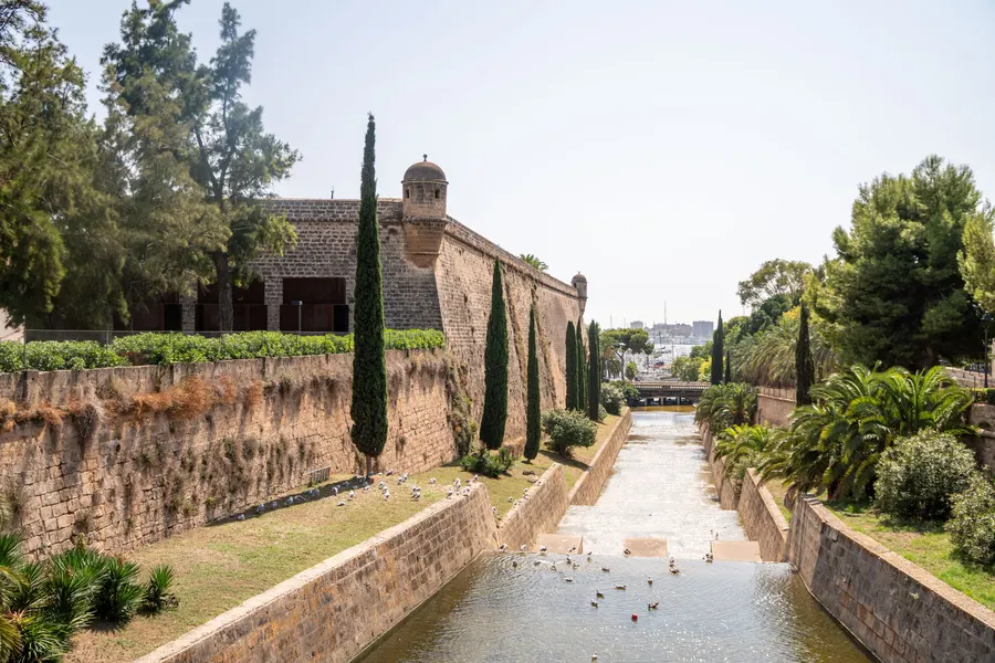 Der kanalisierte Torrent de Sa Riera unterhalb der Bastionsmauer von Es Baluard, mit Zypressen und Enten im Wasser.
