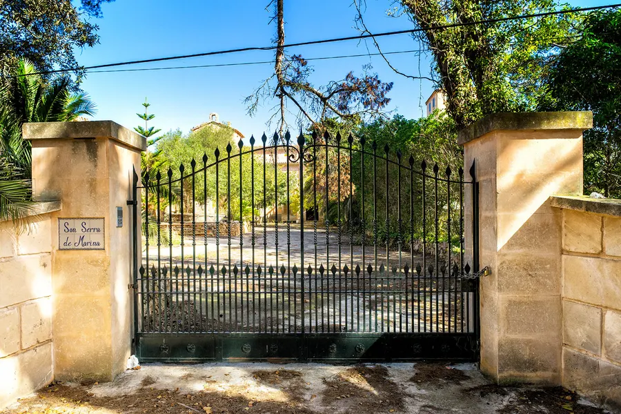 Schmiedeeisernes Tor zwischen zwei Steinpfeilern mit einem Namensschild, dahinter die Zufahrt zum Gut Son Serra de Marina.
