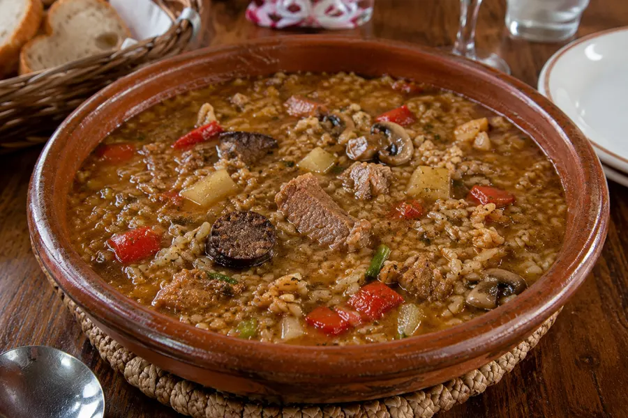 Arròs brut — „Schmutziger Reis": kräftige Reissuppe mit Fleisch, Pilzen, Gemüse. (mit künstlicher Intelligenz erzeugte Abbildung)