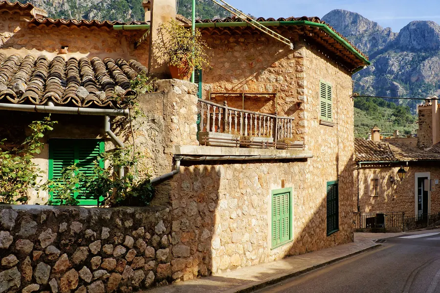 Steinhaus in Fornalutx mit hölzernem Balkon und grünen Fensterläden, dahinter die schroffen Felskämme der Serra de Tramuntana.