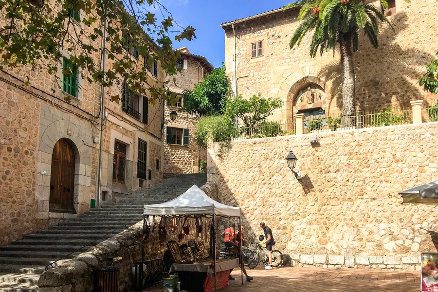 Breite Treppe und Platz in Fornalutx mit einem weißen Marktstandzelt, hoher Natursteinmauer und einer Palme darüber.
