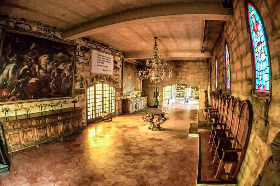 Museumsraum im Obergeschoss von Gordiola mit Gemälde, Kronleuchter, Buntglasfenstern und Vitrinen entlang der Wände.
