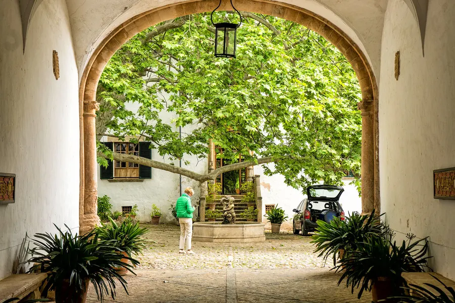 Gewölbter Durchgang zum Innenhof des Herrenhauses von Alfàbia mit Laterne, Kübelpflanzen und einem alten Baum dahinter.