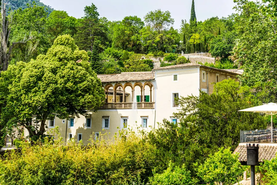 Die Loggia des Herrenhauses von La Granja über dem bewaldeten Garten, davor hohe Bäume und Zypressen.