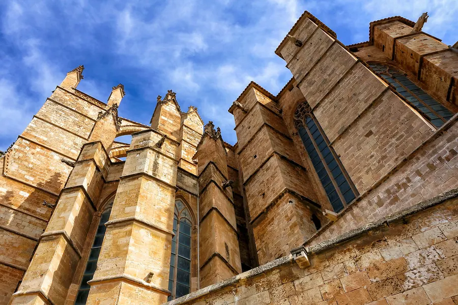 Strebepfeiler und Strebebögen an der Seitenwand der Kathedrale von Palma vor blauem Himmel mit hohen schmalen Fenstern.