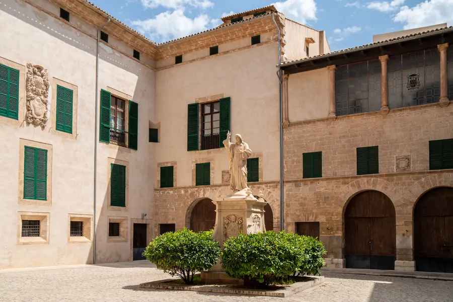Innenhof des Bischofspalasts in Palma mit Arkaden, einer Steinfigur und beschnittenen Buchsbäumen.
