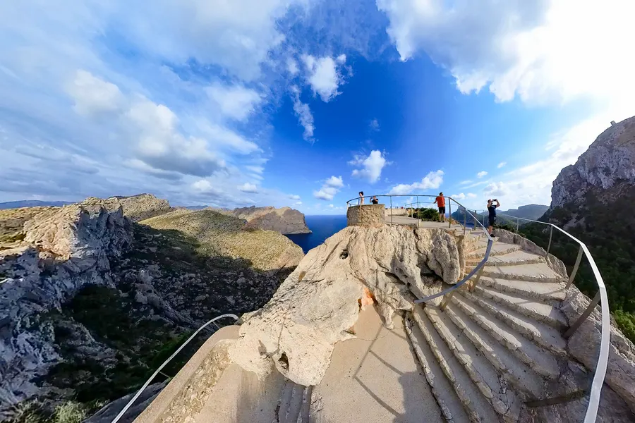 Breite, geschwungene Betontreppe mit Metallgeländer, die über den Fels zu einer Aussichtsplattform mit mehreren Personen hinaufführt; im Hintergrund die gestaffelten Klippen der Nordküste und das Meer.