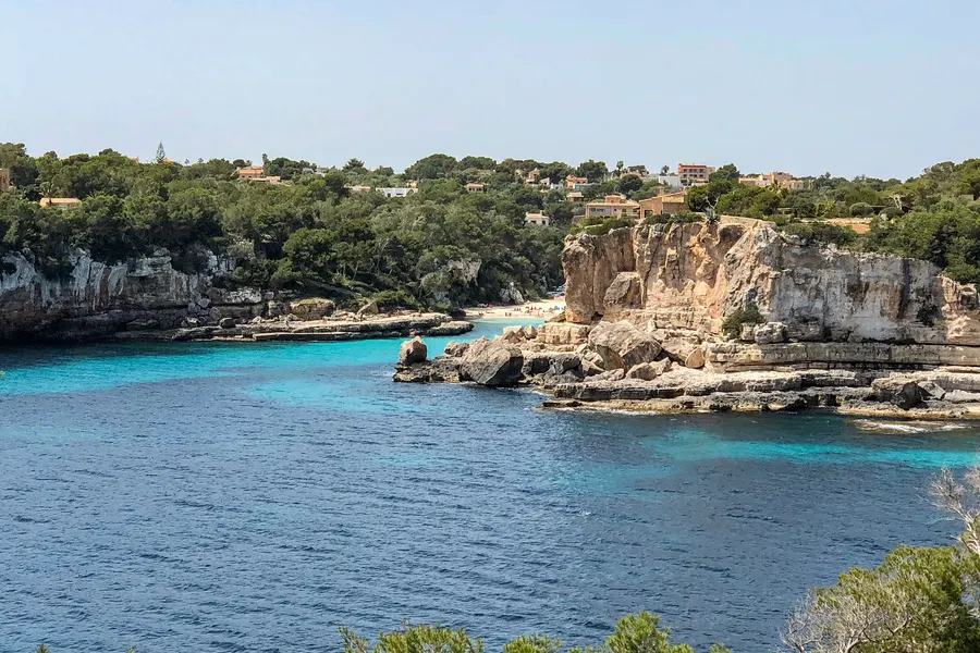 Blick von der Anhöhe über die zerklüftete Küste bei Santanyí mit türkisfarbenem Wasser, hellen Felsen und Kiefern auf den Klippen.