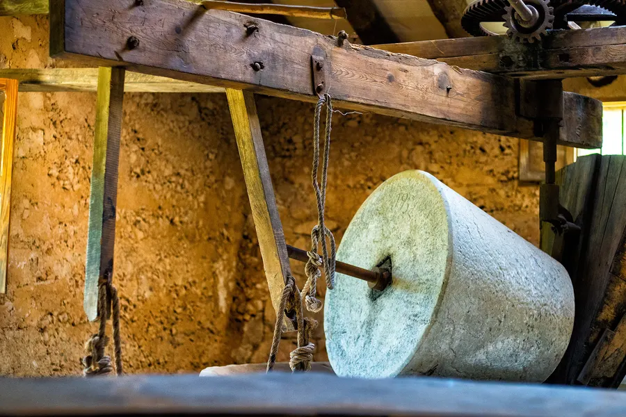 Große steinerne Mahlwalze einer alten Ölpresse unter schweren Holzbalken im Wirtschaftsraum von Miramar.