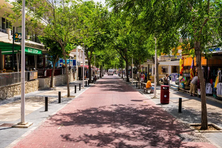 Der Boulevard in Peguera mit rotem Belag, Platanen zu beiden Seiten und Läden und Lokalen im Erdgeschoss.
