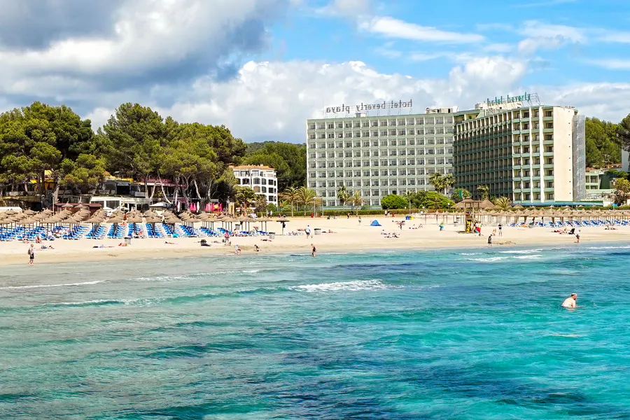 Großer Hotelblock direkt am Sandstrand von Peguera, davor Liegen und das klare Wasser der Bucht.

