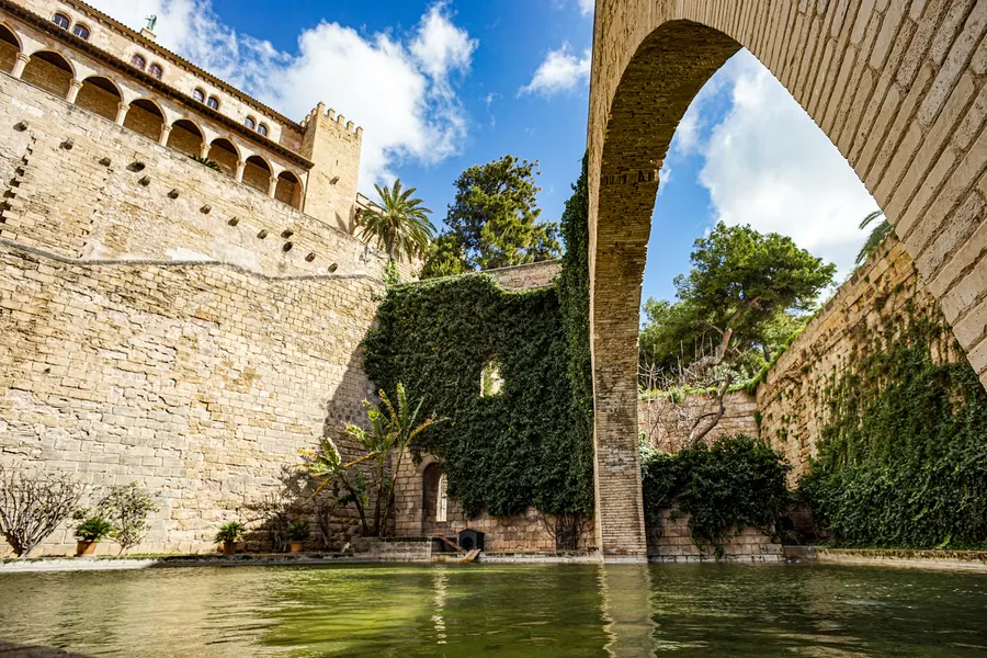 Efeubewachsener Steinbogen über einem grünen Wasserbecken unterhalb der Palastmauer im Königsgarten S'Hort del Rei.