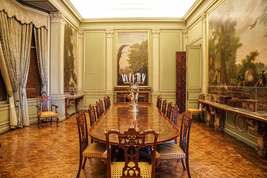 Das Esszimmer des Palau March mit langer polierter Tafel, geschnitzten Stühlen, hellgrün gefassten Wandpaneelen und großformatigen Landschaftsgemälden.