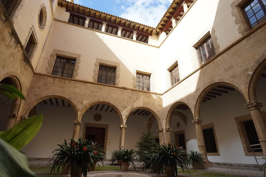 Heller Innenhof eines Altstadthauses in Palma mit Rundbogenarkaden, Säulen und Grünpflanzen in Kübeln.
