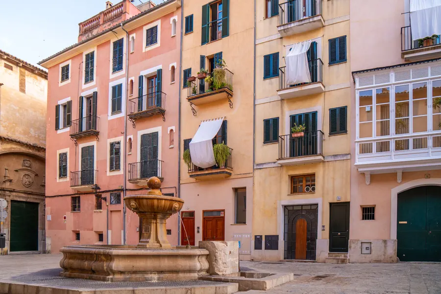 Der kleine Platz Plaça de Sant Jeroni in der Altstadt von Palma mit Kirche, Steinfassaden und einem Brunnen in der Mitte.
